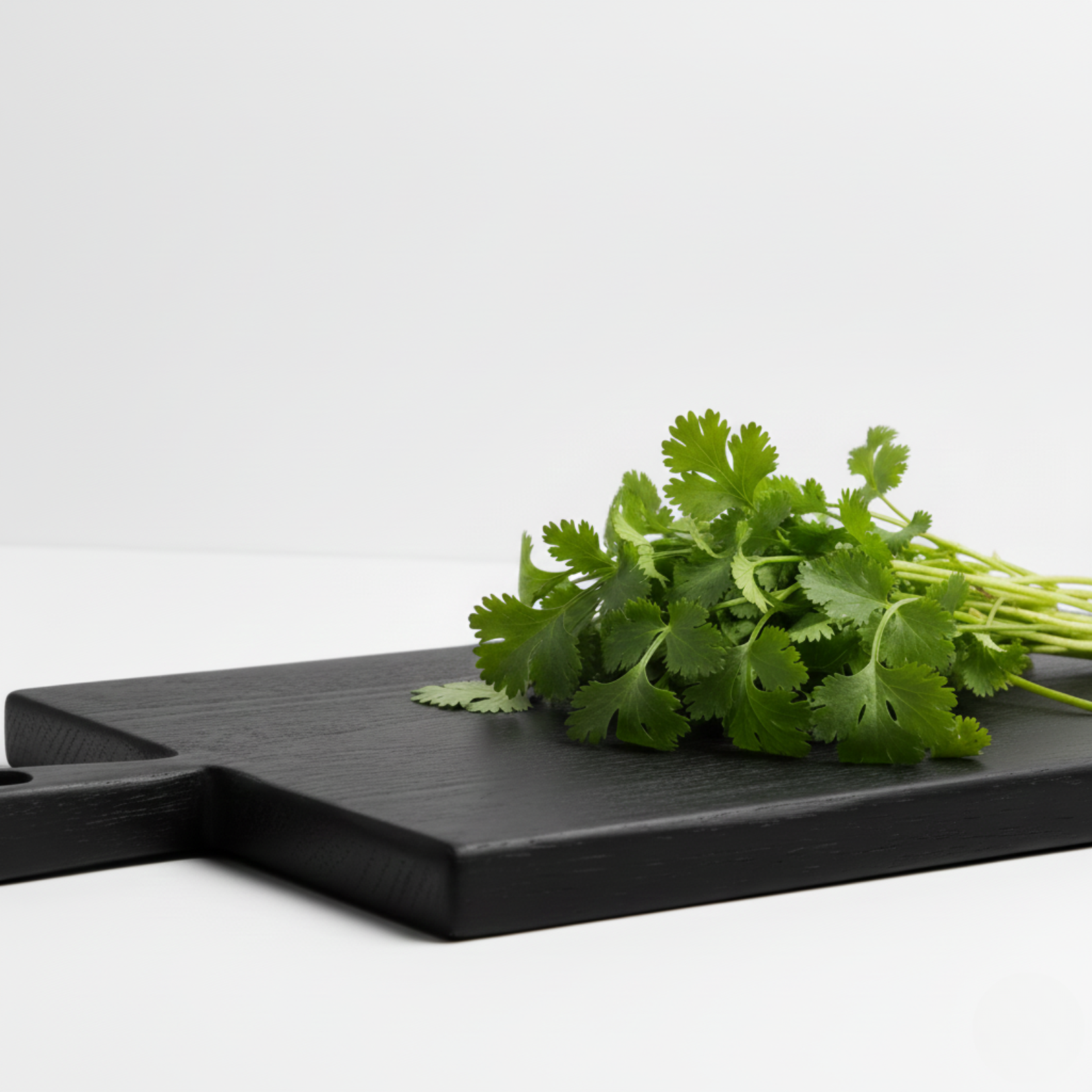 Black wooden cutting board with fresh green herbs on a white background