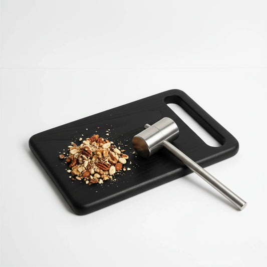 ARTSN charred black rectangular cutting board with handle slot holding chopped nuts and metal mallet on white background