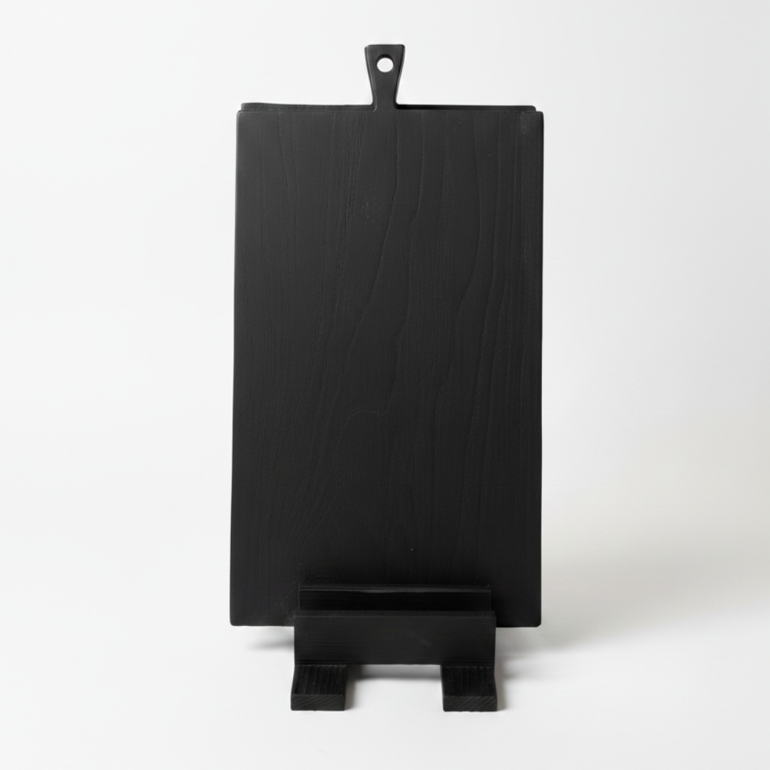 ARTSN black charred cutting board with handle resting on matching stand against white background