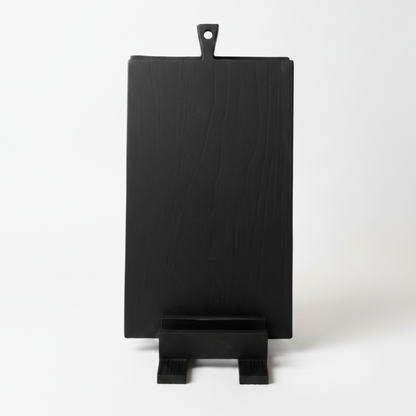 ARTSN black charred cutting board with handle resting on matching stand against white background