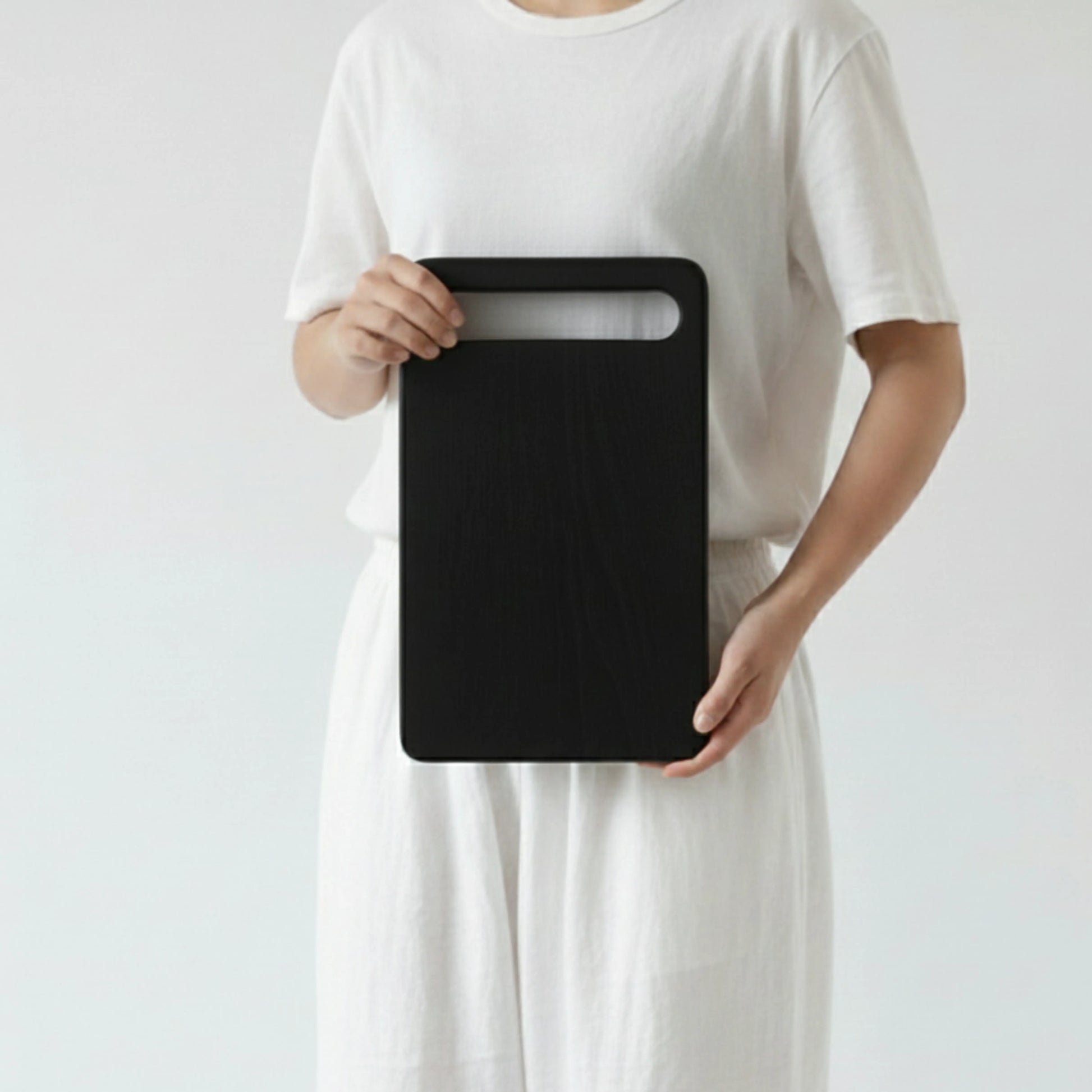 ARTSN charred rectangular cutting board with handle slot held by person in white outfit against plain background