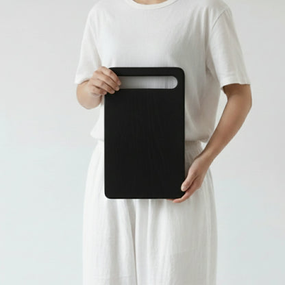 ARTSN charred rectangular cutting board with handle slot held by person in white outfit against plain background