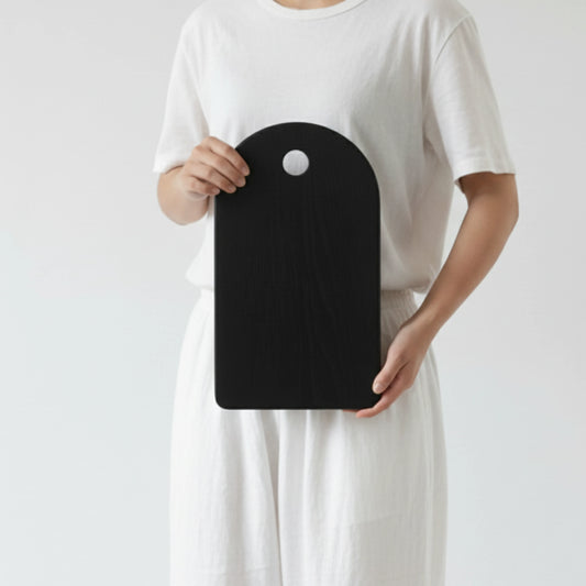 ARTSN charred black rectangular cutting board with round hole handle held by person in white outfit against plain background